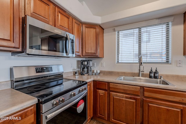 kitchen with stainless steel appliances, a sink, brown cabinetry, and light countertops