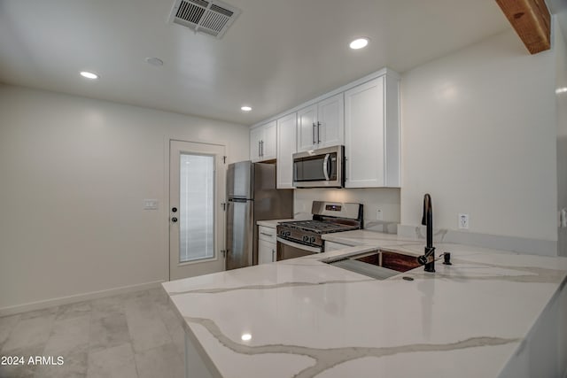 kitchen featuring light stone countertops, stainless steel appliances, kitchen peninsula, and white cabinetry