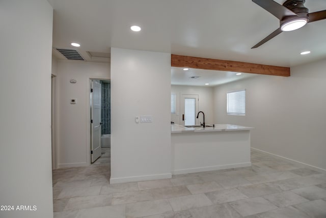 kitchen with light tile flooring, kitchen peninsula, beam ceiling, sink, and ceiling fan