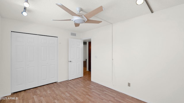 unfurnished bedroom featuring ceiling fan, light wood-type flooring, a textured ceiling, and a closet