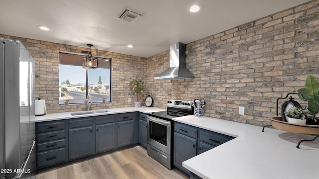 kitchen featuring sink, decorative light fixtures, light hardwood / wood-style floors, stainless steel appliances, and wall chimney exhaust hood