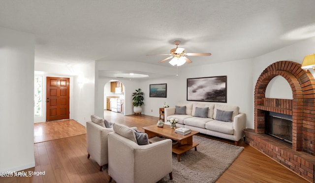 living room with a fireplace, ceiling fan, light hardwood / wood-style floors, and a textured ceiling