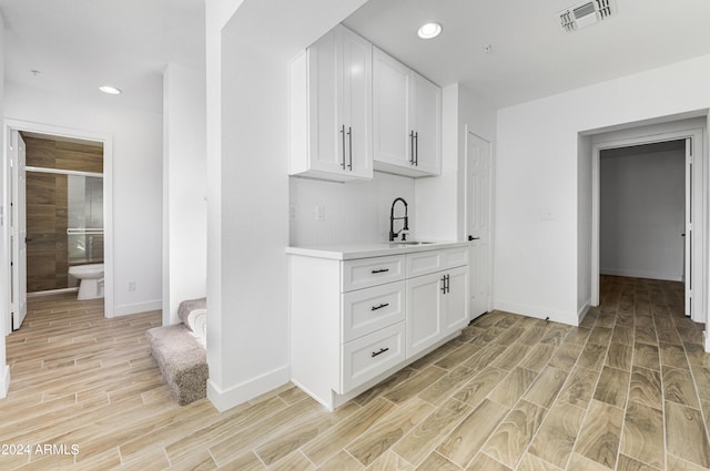 bar featuring white cabinets, light hardwood / wood-style flooring, and sink