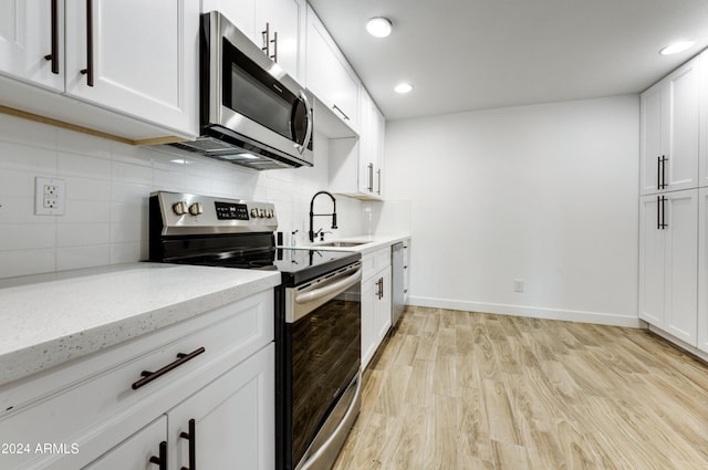 kitchen featuring white cabinets, light stone countertops, light wood-type flooring, and stainless steel appliances