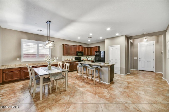 31133 N 132nd Ln, Peoria, AZ 85383 - kitchen with black appliances, a kitchen bar, a center island with sink, recessed lighting, and light stone countertops