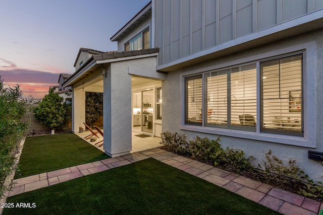 property exterior at dusk featuring a lawn and a patio area