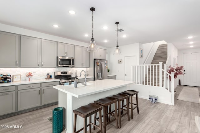 kitchen with appliances with stainless steel finishes, a center island with sink, gray cabinets, and pendant lighting