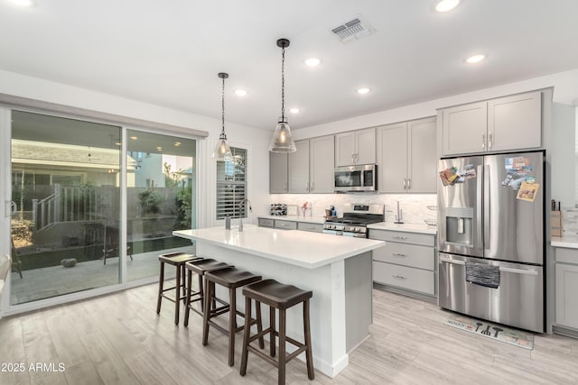 kitchen with gray cabinetry, stainless steel appliances, light hardwood / wood-style flooring, a kitchen bar, and a kitchen island with sink