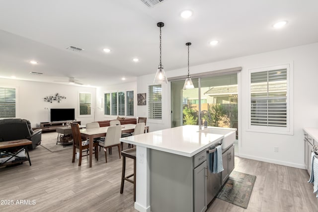 kitchen featuring decorative light fixtures, a center island with sink, light hardwood / wood-style floors, and sink