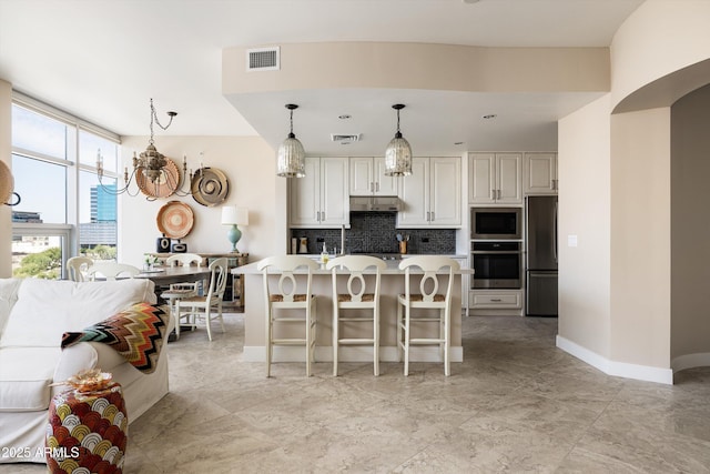 kitchen with stainless steel appliances, backsplash, under cabinet range hood, a breakfast bar, and decorative light fixtures