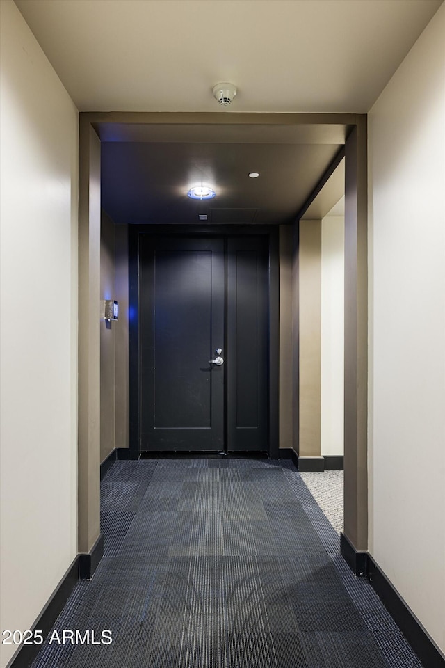 corridor featuring baseboards and dark colored carpet