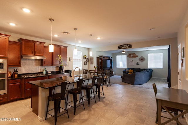 19937 W Heatherbrae Dr, Litchfield Park, AZ 85340 - kitchen with under cabinet range hood, stainless steel appliances, a breakfast bar area, a sink, and decorative backsplash