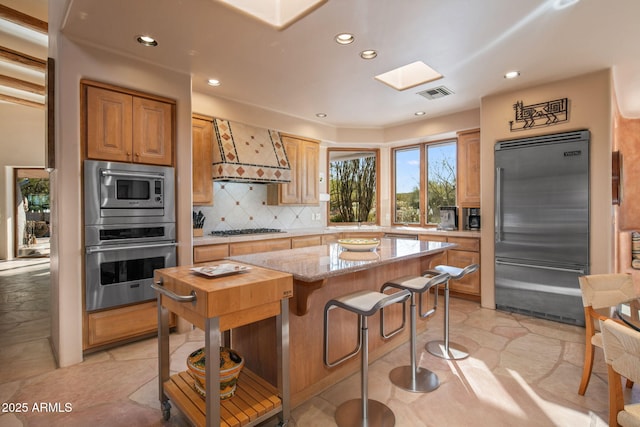 kitchen featuring premium range hood, a skylight, backsplash, a center island, and built in appliances