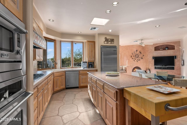 kitchen with appliances with stainless steel finishes, a skylight, sink, a center island, and ceiling fan