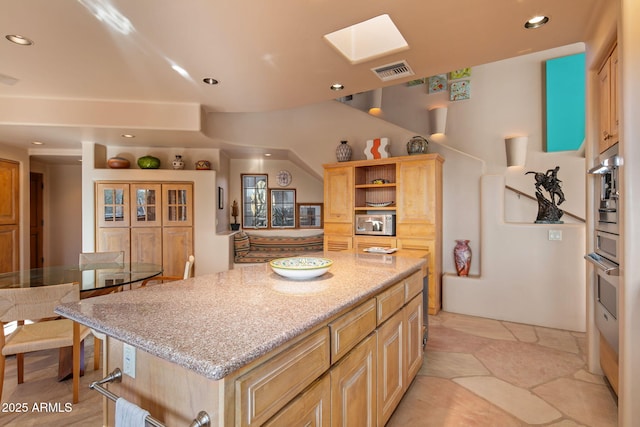 kitchen with light brown cabinetry, a skylight, light stone countertops, and a kitchen island