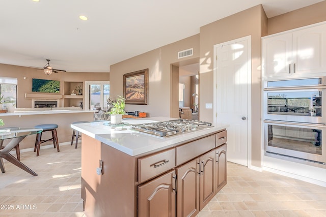 10772 E Running Deer Trl, Scottsdale, AZ 85262 - kitchen with a ceiling fan, a fireplace, appliances with stainless steel finishes, a center island, and light countertops