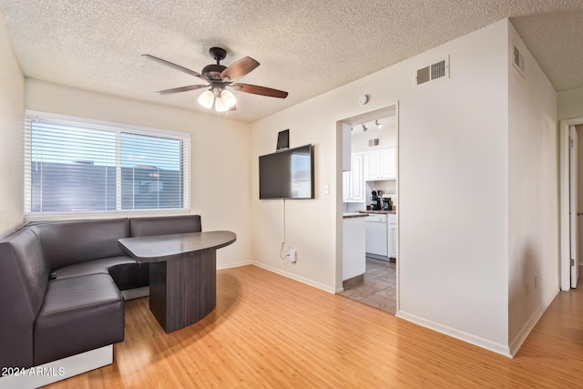 living room featuring a textured ceiling, light wood-type flooring, and ceiling fan