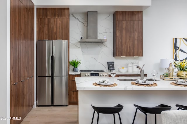 kitchen featuring wall chimney range hood, sink, stainless steel refrigerator, and a kitchen bar