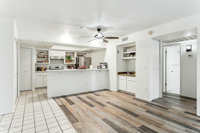 kitchen with stainless steel refrigerator, stove, white cabinets, kitchen peninsula, and ceiling fan