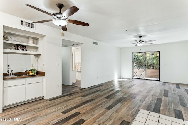 unfurnished living room with wood-type flooring, indoor wet bar, built in shelves, and ceiling fan