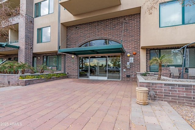 view of exterior entry with a patio area, brick siding, and stucco siding