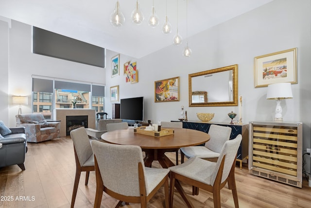 dining room featuring a towering ceiling, beverage cooler, a fireplace, and light wood finished floors