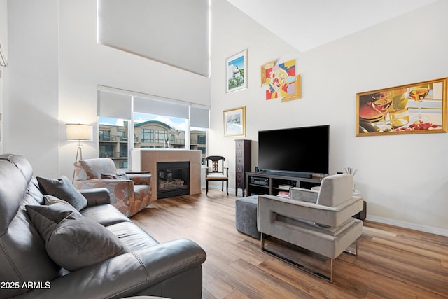 living area featuring a glass covered fireplace, a high ceiling, baseboards, and wood finished floors