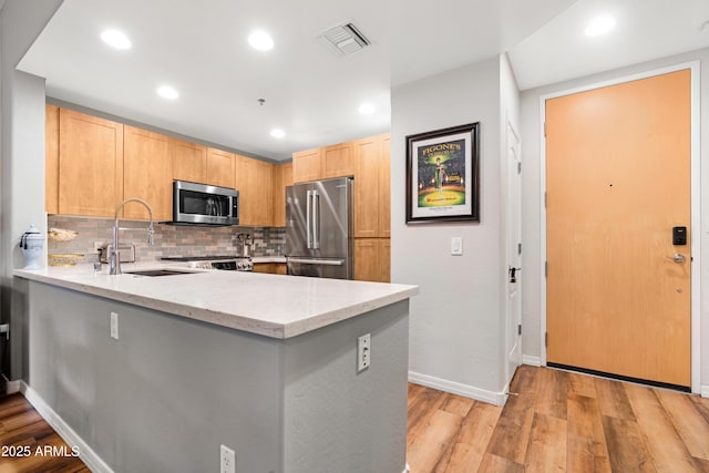 kitchen featuring light stone counters, appliances with stainless steel finishes, kitchen peninsula, and light hardwood / wood-style flooring