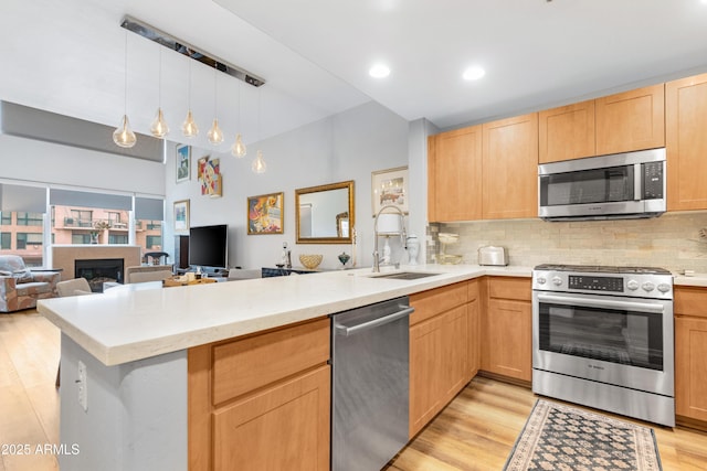 kitchen featuring light brown cabinets, a peninsula, a sink, decorative backsplash, and appliances with stainless steel finishes