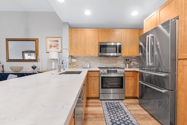 kitchen with tasteful backsplash, light stone countertops, light wood-type flooring, appliances with stainless steel finishes, and a sink