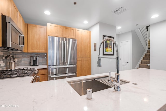 kitchen with sink, light brown cabinets, appliances with stainless steel finishes, light stone countertops, and decorative backsplash