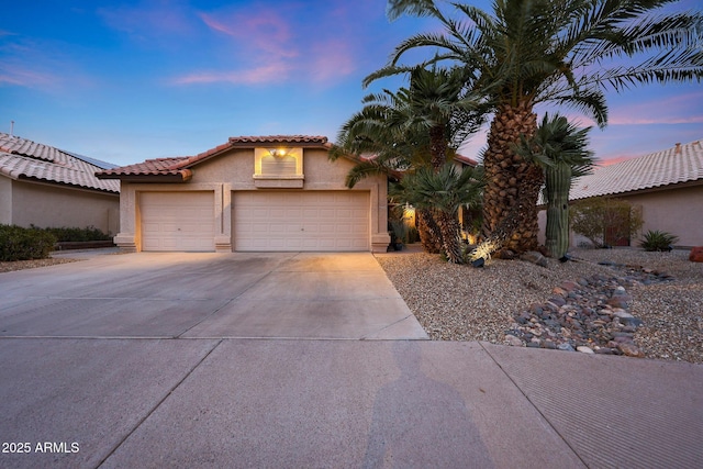 mediterranean / spanish-style home with a garage, concrete driveway, a tiled roof, and stucco siding