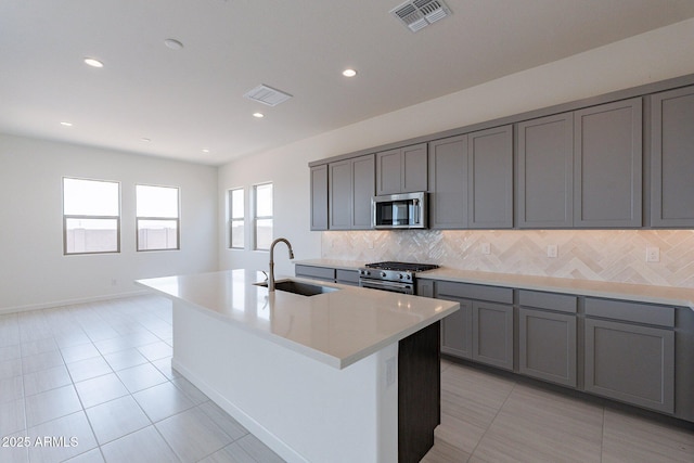 kitchen featuring tasteful backsplash, stainless steel appliances, sink, a center island with sink, and light tile patterned flooring