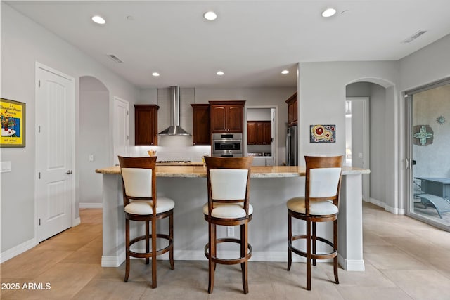 1385 Ridgewood Dr, Prescott, AZ 86305 - kitchen featuring arched walkways, wall chimney exhaust hood, appliances with stainless steel finishes, recessed lighting, and a kitchen bar