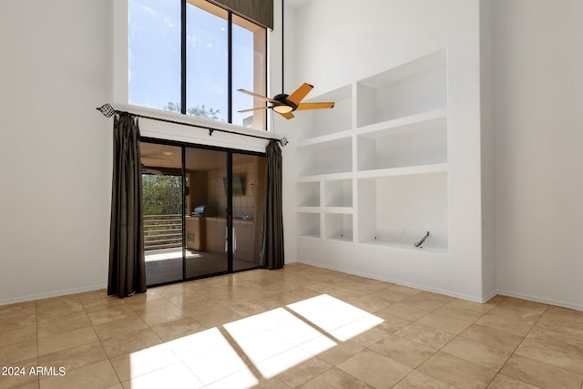 tiled spare room featuring a high ceiling, ceiling fan, and built in shelves