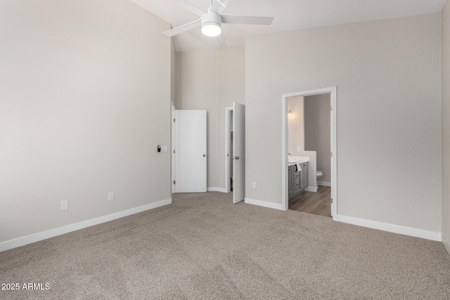 unfurnished bedroom featuring light colored carpet, connected bathroom, a high ceiling, and ceiling fan