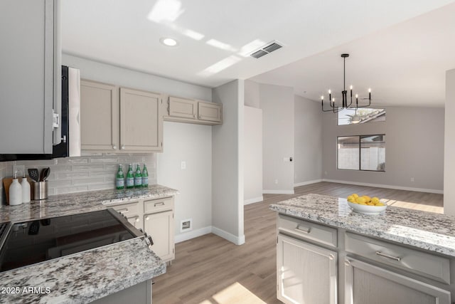 kitchen featuring backsplash, light hardwood / wood-style flooring, light stone countertops, and hanging light fixtures