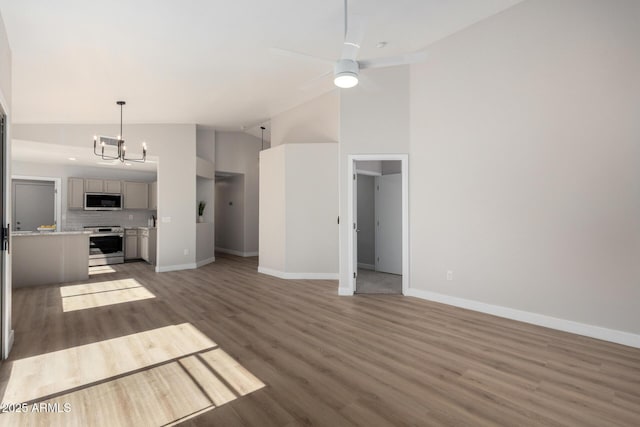 unfurnished living room with ceiling fan with notable chandelier, dark wood-type flooring, and high vaulted ceiling