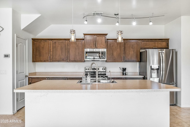 kitchen featuring light tile patterned flooring, sink, hanging light fixtures, appliances with stainless steel finishes, and a kitchen island with sink