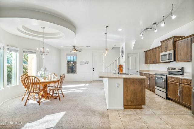 kitchen with sink, hanging light fixtures, appliances with stainless steel finishes, a tray ceiling, and a kitchen island with sink