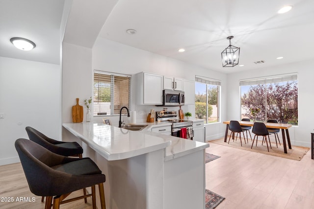 kitchen with sink, kitchen peninsula, pendant lighting, stainless steel appliances, and white cabinets