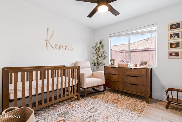 bedroom with a crib, ceiling fan, and light hardwood / wood-style floors