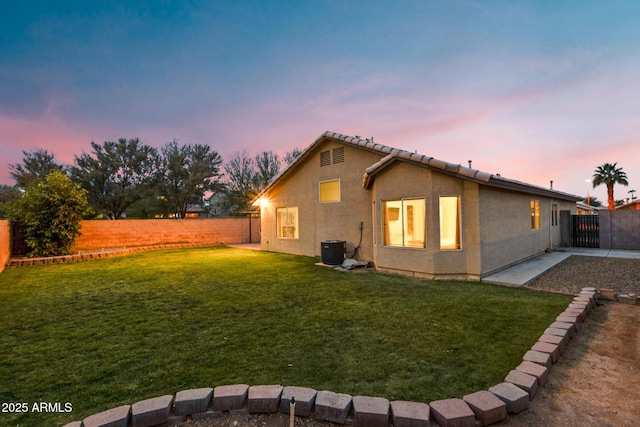 back house at dusk featuring a yard and cooling unit