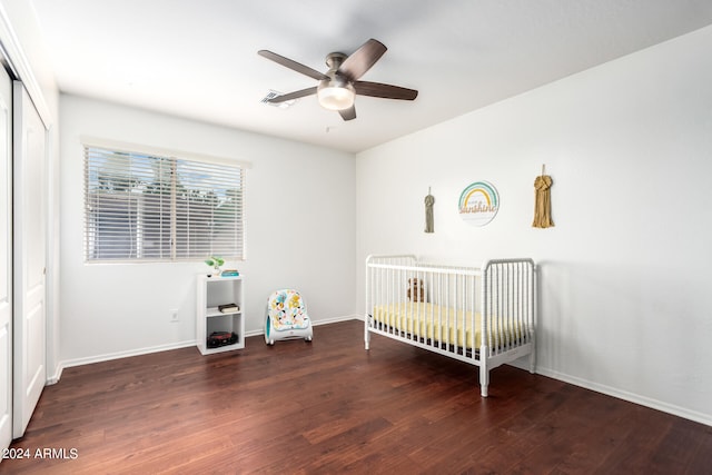 unfurnished bedroom with a nursery area, ceiling fan, a closet, and dark hardwood / wood-style flooring