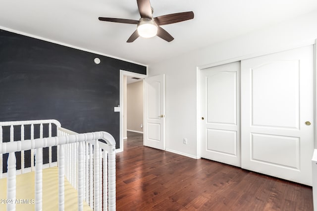 unfurnished bedroom featuring a nursery area, ceiling fan, dark hardwood / wood-style floors, and a closet