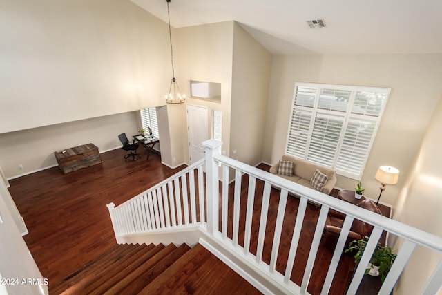 stairway with high vaulted ceiling, wood-type flooring, and a chandelier