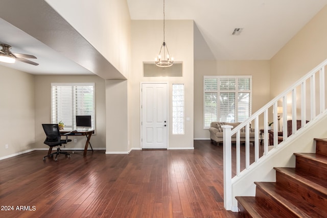 entryway with plenty of natural light, a towering ceiling, ceiling fan with notable chandelier, and dark wood-type flooring