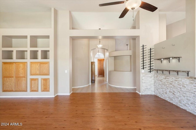 unfurnished living room with built in shelves, hardwood / wood-style floors, high vaulted ceiling, and ceiling fan