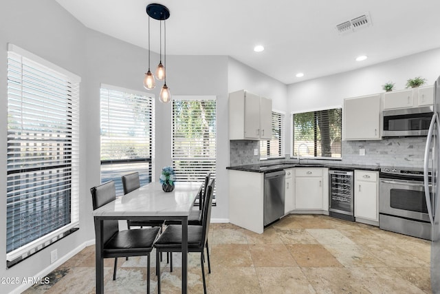 kitchen with appliances with stainless steel finishes, wine cooler, a wealth of natural light, decorative backsplash, and decorative light fixtures