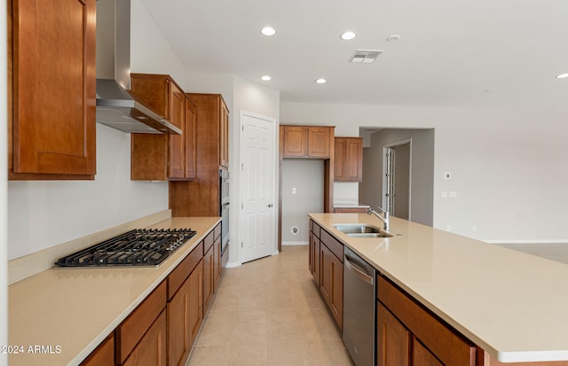 kitchen featuring wall chimney range hood, light tile patterned floors, appliances with stainless steel finishes, an island with sink, and sink